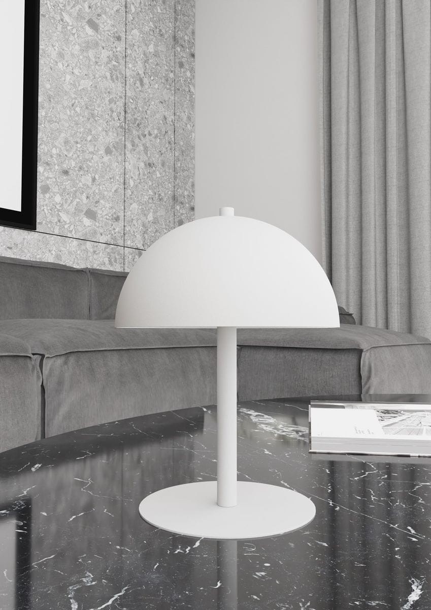 Lampa stołowa Mogu w kolorze białym, z okrągłym kloszem, umieszczona na okrągłej podstawie. Produkt prezentowany na marmurowym stole w otoczeniu szarego sofy i zasłon. Ujęcie z boku, pokazujące minimalistyczny design.