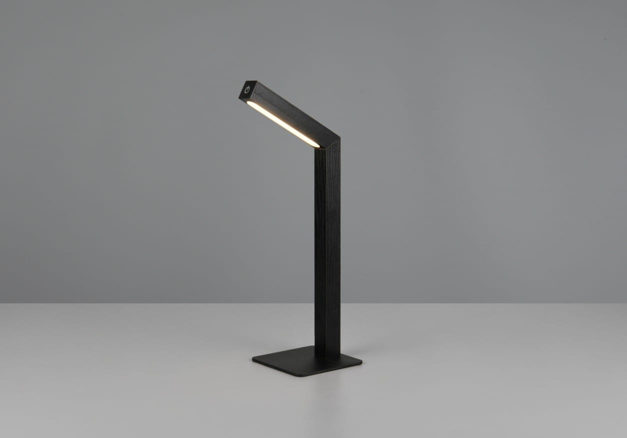 Lampa stołowa bezprzewodowa Skip w kolorze czarnym, z prostokątną podstawą. Posiada wbudowane źródło światła LED o mocy 2W, ustawiona pod kątem. Tło jednolite, szare, podkreślające minimalistyczny design.