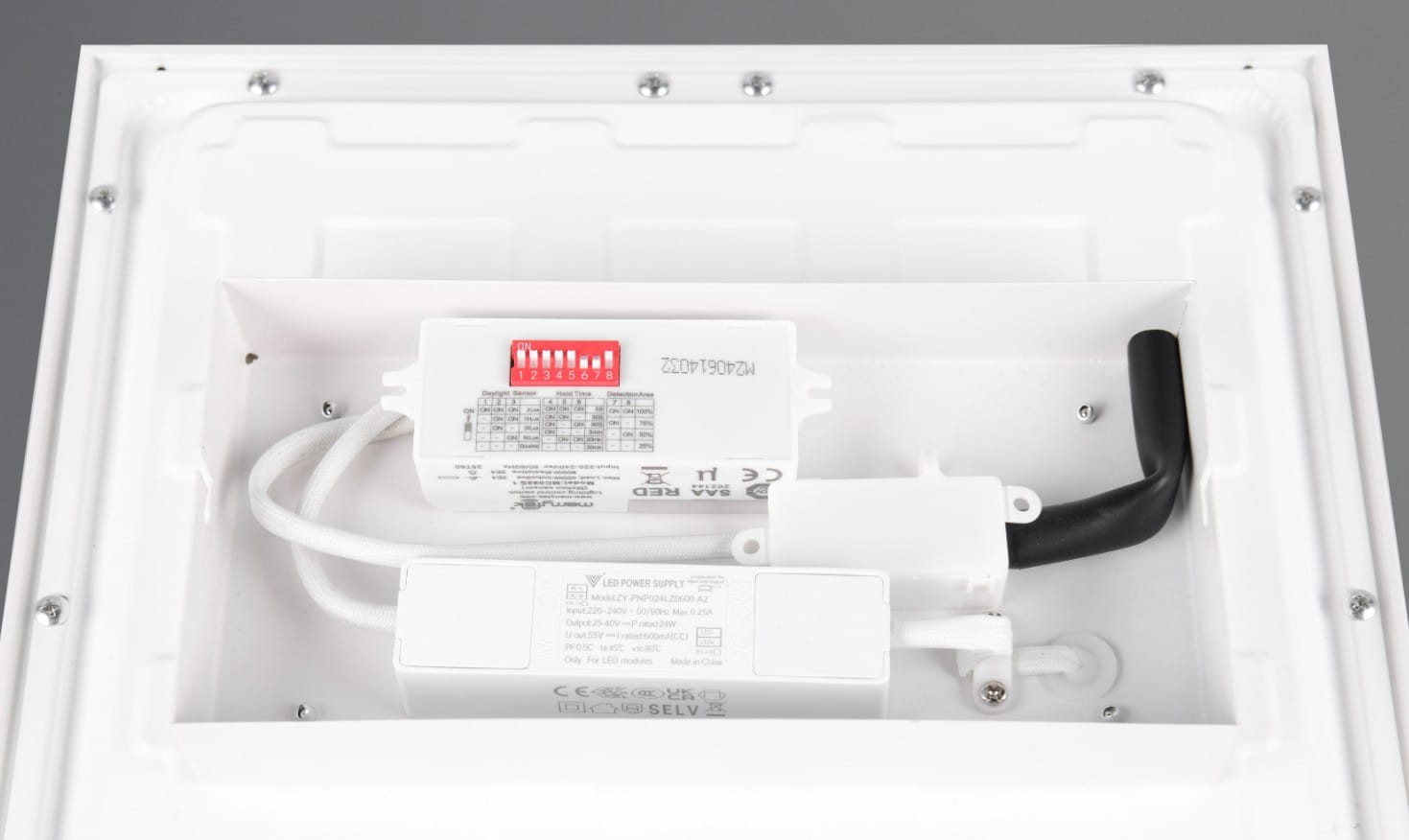 Plafon Sirius z czujnikiem ruchu w kolorze białym, z widocznymi elementami instalacyjnymi, w tym zasilaczem LED oraz przewodami. Ujęcie z góry, pokazujące wnętrze lampy, z wyraźnymi oznaczeniami technicznymi.