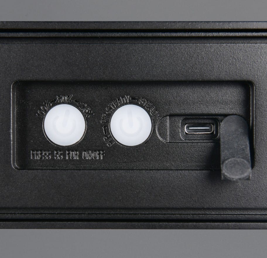 Czarny kinkiet zewnętrzny Silves Hybrid z przyciskami włączania oraz portem USB do ładowania. Widoczne dwa okrągłe przyciski oraz przesuwany przełącznik. Design minimalistyczny, idealny do użytku na zewnątrz, z klasą ochrony IP44.
