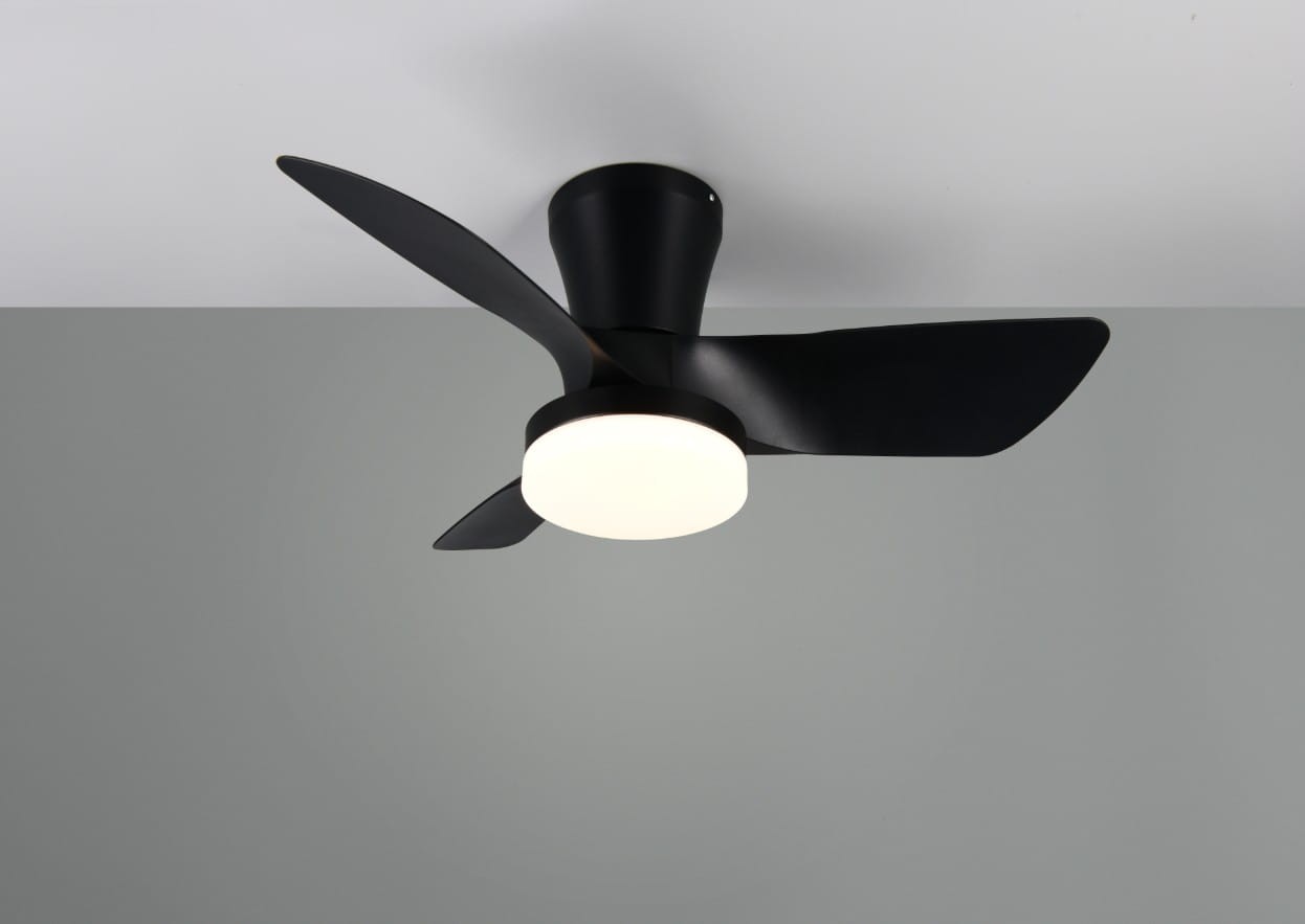 Lampa sufitowa Randers z wentylatorem, czarna, z okrągłą, białą oprawą LED. Posiada trzy skrzydła wentylatora. Zamontowana na suficie, widok z dołu. Pilot do zdalnego sterowania. Tło w odcieniach szarości.