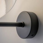 Kinkiet Memory w kolorze czarnym, z oprawą na żarówkę E14. Widoczny jest okrągły uchwyt montażowy oraz prosty, cienki ramion. Produkt zamontowany na ścianie, w bliskim ujęciu.