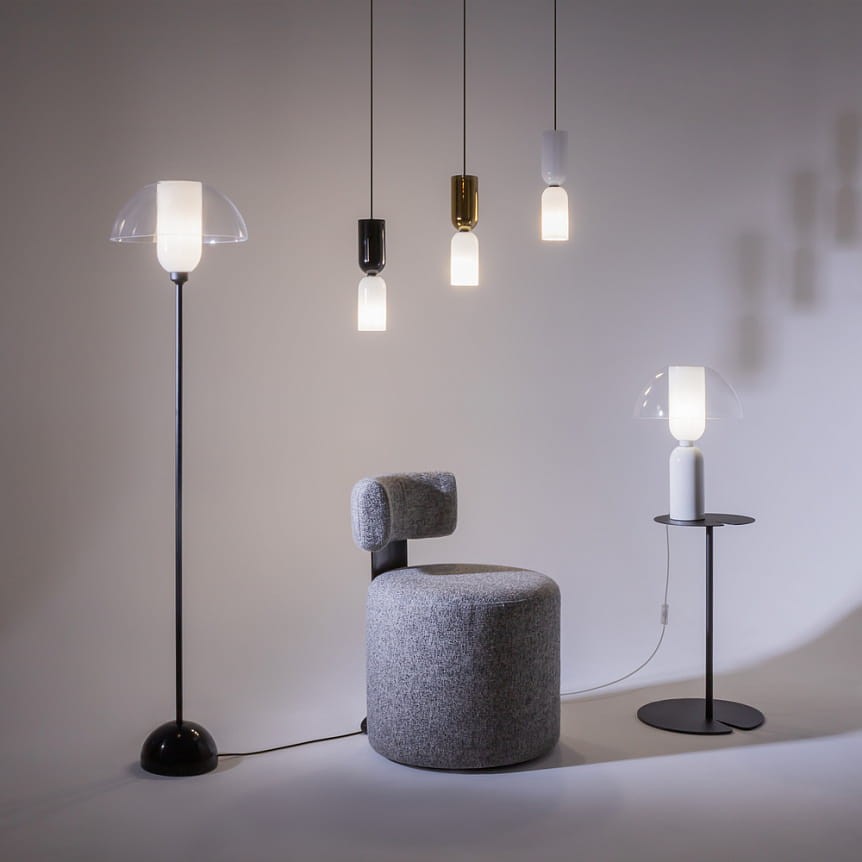 Lampa wisząca Memory 1xE14 w kolorze białym, o cylindrycznym kształcie z przezroczystym kloszem. Zawieszona na cienkim przewodzie, w otoczeniu innych lamp i nowoczesnych mebli. Tło jasne, minimalistyczne.