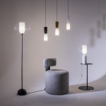 Lampa wisząca Memory 1xE14 w kolorze białym, o cylindrycznym kształcie z przezroczystym kloszem. Zawieszona na cienkim przewodzie, w otoczeniu innych lamp i nowoczesnych mebli. Tło jasne, minimalistyczne.