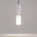 Wisząca lampa Memory z jednym gniazdem E14, w kolorze białym. Składa się z gładkiego, błyszczącego abażura oraz matowego klosza, emitującego ciepłe światło. Produkt zawieszony na czarnym przewodzie, na jednolitym tle.