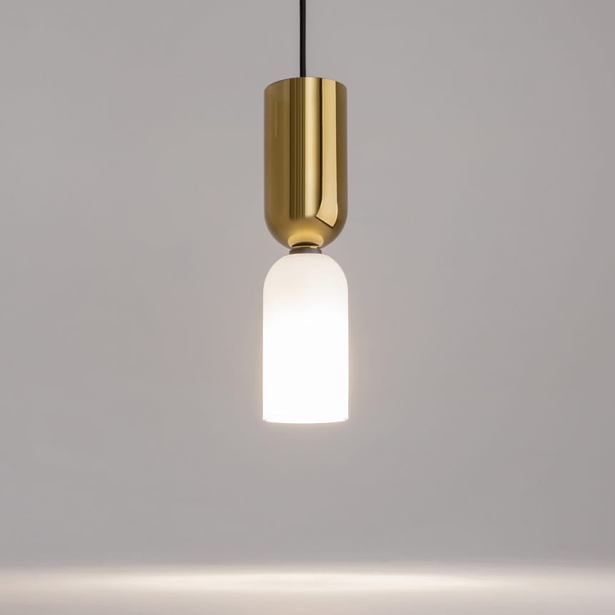 Lampa wisząca Memory w kolorze złotym z jedną oprawą na żarówkę E14. Posiada cylindryczny, błyszczący klosz u góry oraz matowy, szklany klosz na dole, emitujący ciepłe światło. Zawieszona na czarnym przewodzie, w minimalistycznym stylu.