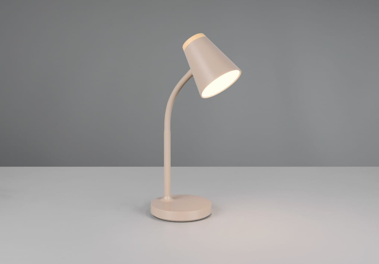 Beżowa lampa biurkowa Pongo z kloszem o stożkowym kształcie, zamontowana na giętkim ramieniu. Ustawiona na okrągłej podstawie, włączona, emitująca ciepłe światło. Tło w odcieniach szarości, prostota aranżacji.