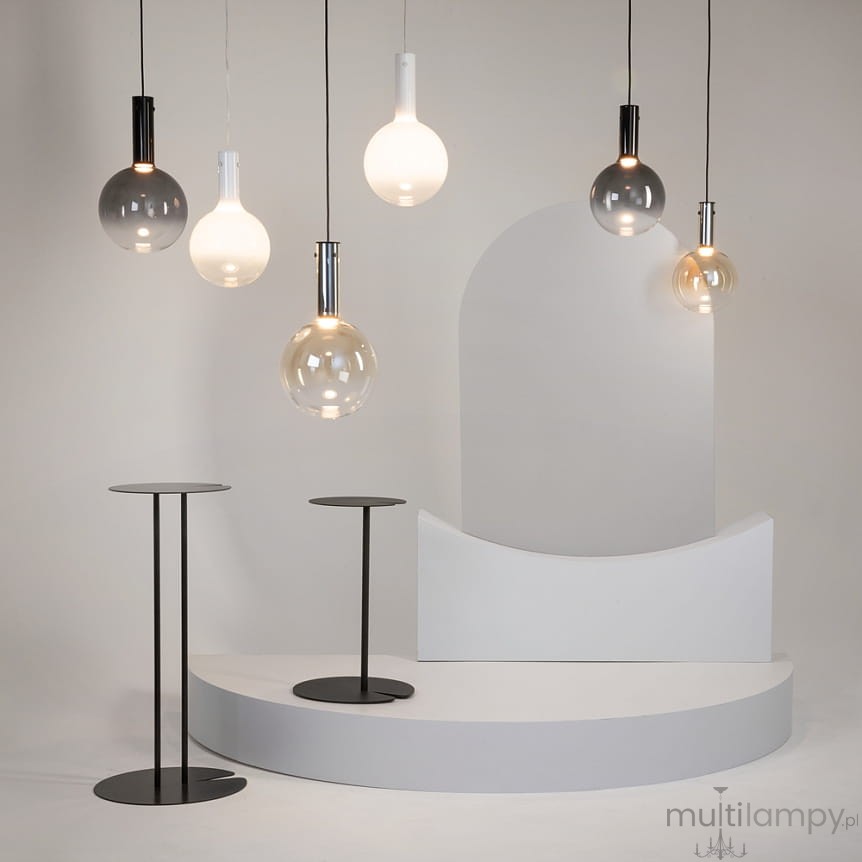 Lampa wisząca Nebula D20 w białej obudowie, z pojedynczym źródłem światła LED 4W. Okrągła, szklana kula w różnych odcieniach, zawieszona na cienkim przewodzie. W tle minimalistyczna aranżacja z czarnymi stolikami i białymi elementami.
