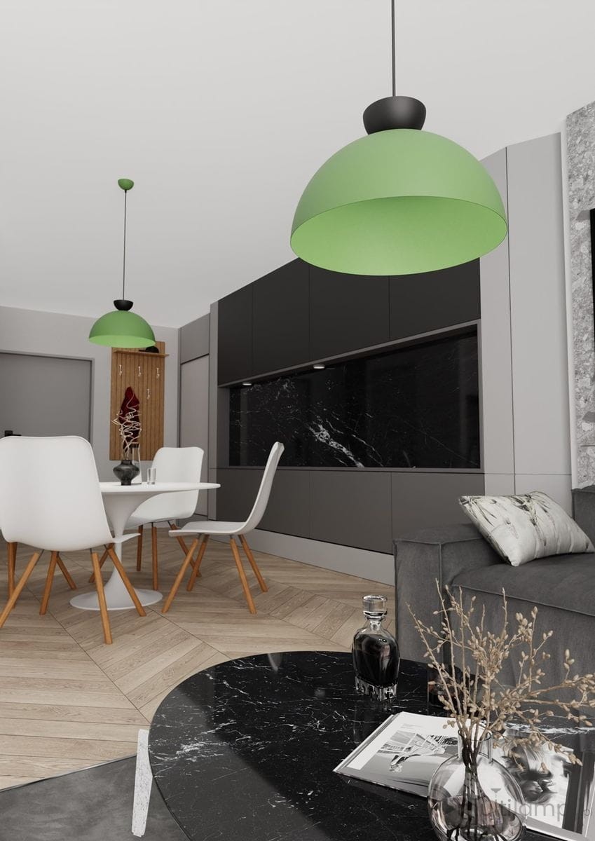 Lampa wisząca Lunaro L w kolorze zielonym z mocowaniem w kolorze czarnym, umieszczona w nowoczesnej kuchni, zawieszona nad okrągłym stołem z białym blatem i drewnianymi nogami. W tle ciemne szafki i marmurowa ściana.