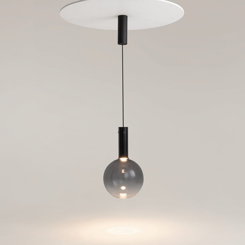 Lampa wisząca Nebula D25 z czarnym metalowym uchwytem i szklanym kloszem w kształcie kuli, zawieszona na cienkim przewodzie. Źródło światła LED o mocy 6W, montowana do sufitu. Tło jasne, minimalistyczne.