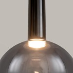 Lampa wisząca Nebula D25 o czarnej wykończeniu z jedną żarówką LED 6W. Ujęcie z bliska, pokazujące gładką, okrągłą czaszę i metalowy uchwyt. Światło wydobywa się z wnętrza, tworząc subtelny efekt oświetleniowy. Tło jasnoszare.