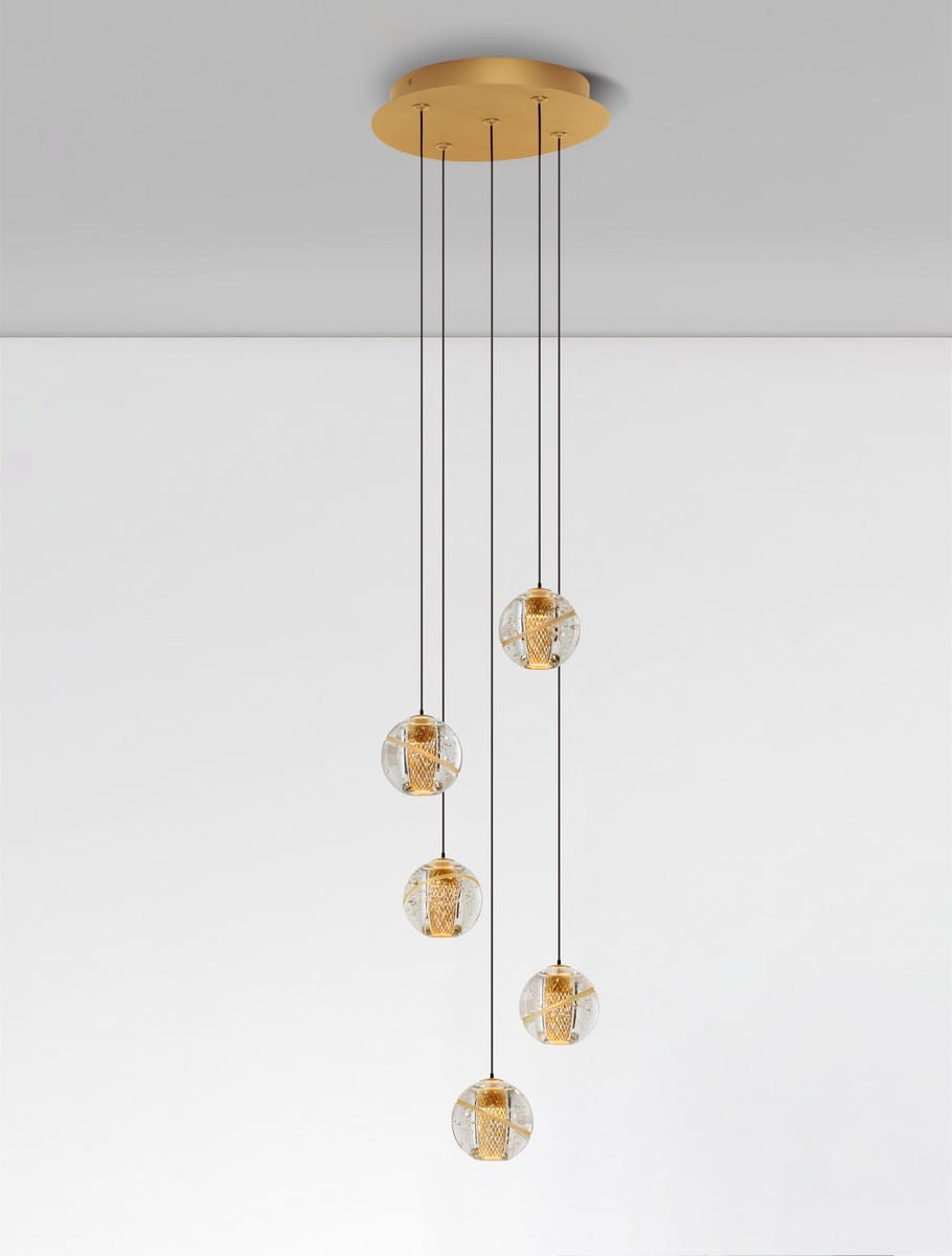 Lampa wisząca Cuyo z pięcioma żarówkami LED, złota podstawa z okrągłym mocowaniem, pięć szklanych kloszy w formie kul, z ozdobnym złotym wnętrzem, zawieszone na cienkich, czarnych linkach, na jasnym tle.