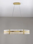 Lampa wisząca Mayo D90 z jedną żarówką LED 45W w złotej oprawie. Posiada półokrągły kształt, z przezroczystymi elementami szklanymi ułożonymi w rzędy. Zawieszona na dwóch cienkich linkach, montowana do sufitu. Tło w jasnoszarym kolorze.