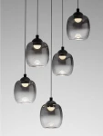Lampa wisząca Toay z pięcioma kloszami LED o mocy 28W, w kolorze czarnym. Klosze mają transparentny, lekko przyciemniony wygląd, zawieszone na czarnych linkach, emitując ciepłe światło. Ujęcie frontalne.