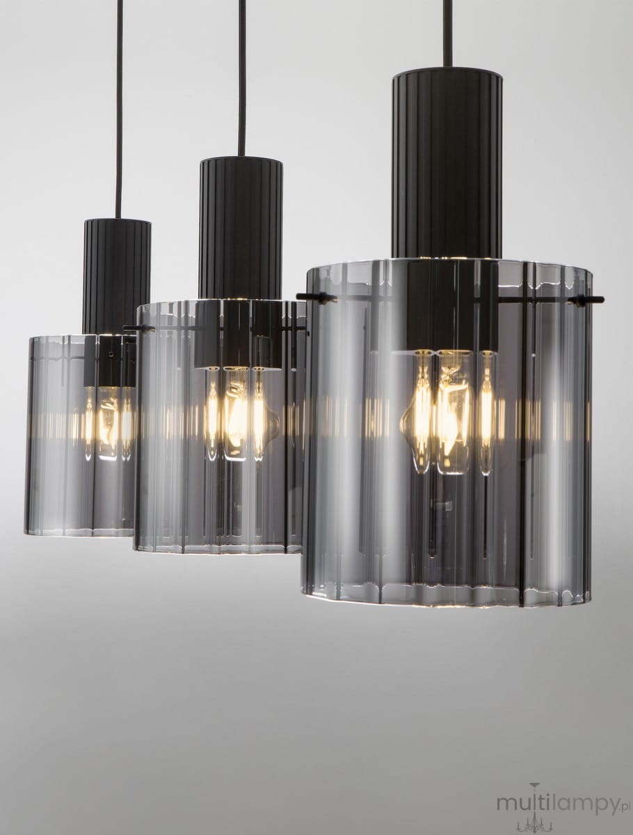 Lampa wisząca Oran z trzema oprawami E27. Czarny metalowy element górny z prążkowaną teksturą, przezroczyste szklane klosze w odcieniu szaro-czarnym, zawieszone na czarnych przewodach. Ujęcie z przodu, ukazujące wszystkie trzy klosze.