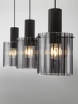 Lampa wisząca Oran z trzema oprawami E27. Czarny metalowy element górny z prążkowaną teksturą, przezroczyste szklane klosze w odcieniu szaro-czarnym, zawieszone na czarnych przewodach. Ujęcie z przodu, ukazujące wszystkie trzy klosze.