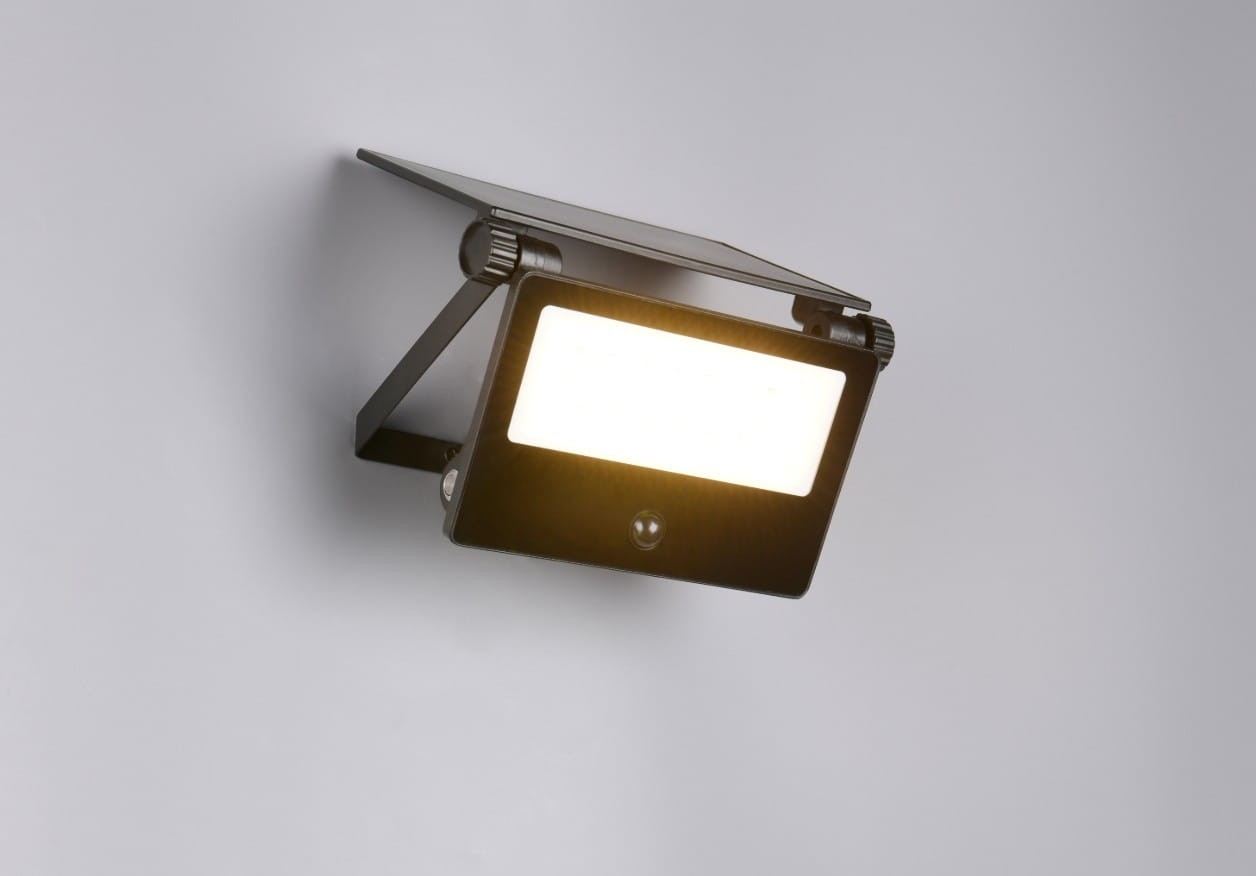 Czarny kinkiet zewnętrzny Moura z czujnikiem ruchu, wyposażony w diodę LED 18W. Ujęcie z boku, produkt zamontowany na ścianie, z widocznym panelem solarnym na górze i białą, prostokątną powierzchnią świecącą.