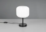 Lampa stołowa Madeline z białym kloszem w kształcie walca na czarnej podstawie. Ujęcie z boku, widoczny kabel z włącznikiem. Klosz ma delikatną fakturę, a całość ma nowoczesny design, idealna do wnętrz.