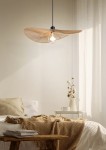 Lampa wisząca Laurine w kolorze czarnym i brązowym, z materiałowym kloszem w kształcie fali, zawieszona na czarnym przewodzie. Widoczna żarówka E27. Lampa znajduje się nad łóżkiem w jasnym wnętrzu z dekoracjami w stylu skandynawskim.