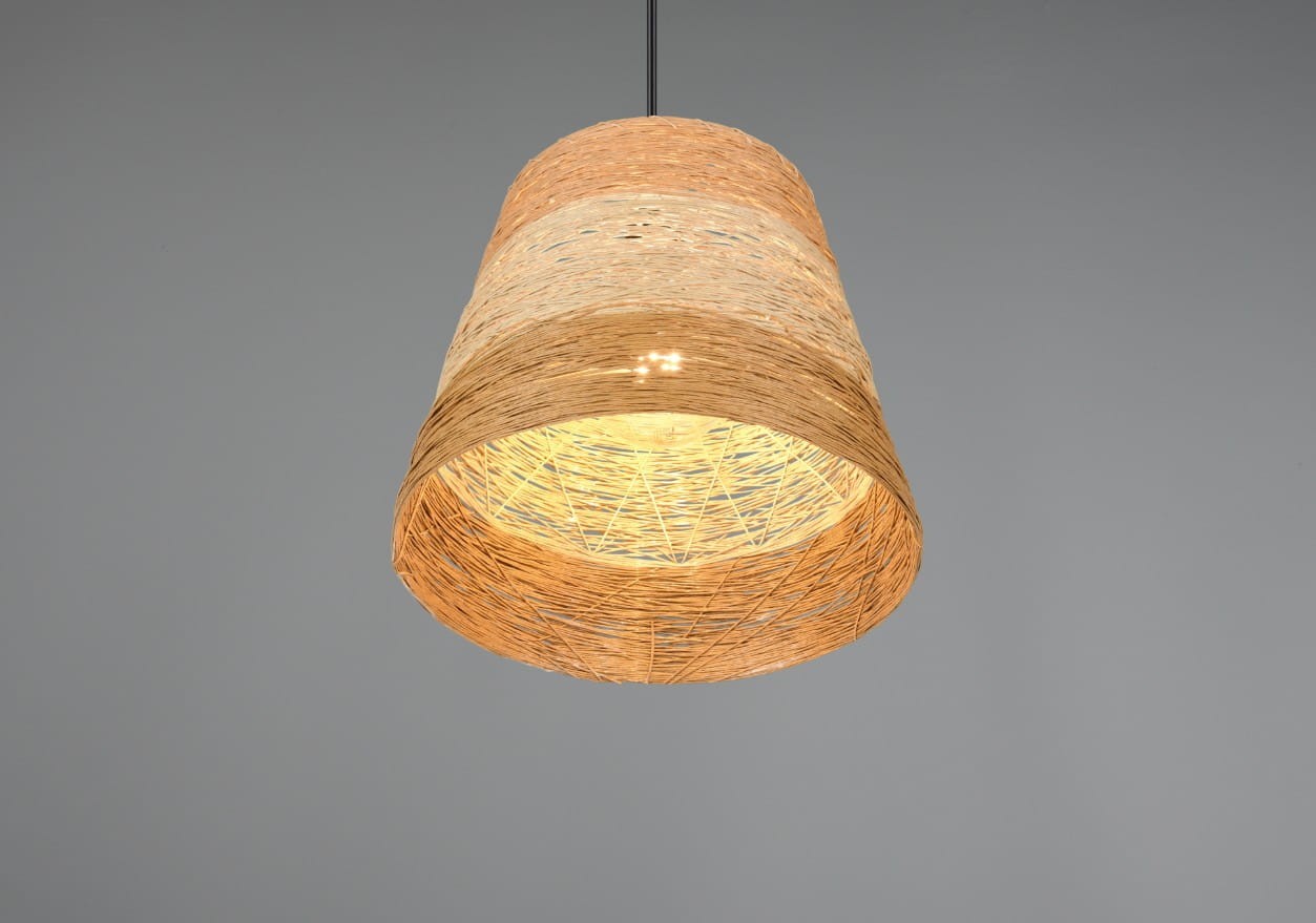 Lampa wisząca Joeline z kloszem w kolorze brązowym, wykonana z plecionego materiału. Posiada okrągły kształt i jest zawieszona na czarnym przewodzie. Wnętrze klosza jest jasne, co zapewnia ciepłe światło. Tło w jednolitym, szarym kolorze.