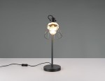 Czarna lampa stołowa Jarome z oprawą E27, stojąca na okrągłej podstawie. Posiada metalowy klosz w formie siatki, eksponujący żarówkę. Przewód z włącznikiem na płaskiej powierzchni, tło w odcieniu szarości.