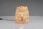 Lampa stołowa Jean w kształcie owalnym, wykonana z naturalnego materiału, w kolorze czarnym i naturalnym. Ujęcie z boku, widoczny kabel z włącznikiem. Światło emitowane przez plecionkę tworzy efektowne cienie.