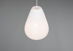 Lampa wisząca Janine w kolorze białym, o kształcie kropli, wykonana z materiału teksturowanego. Zawieszona na białym przewodzie, widoczna żarówka E27. Tło szare, minimalistyczne.