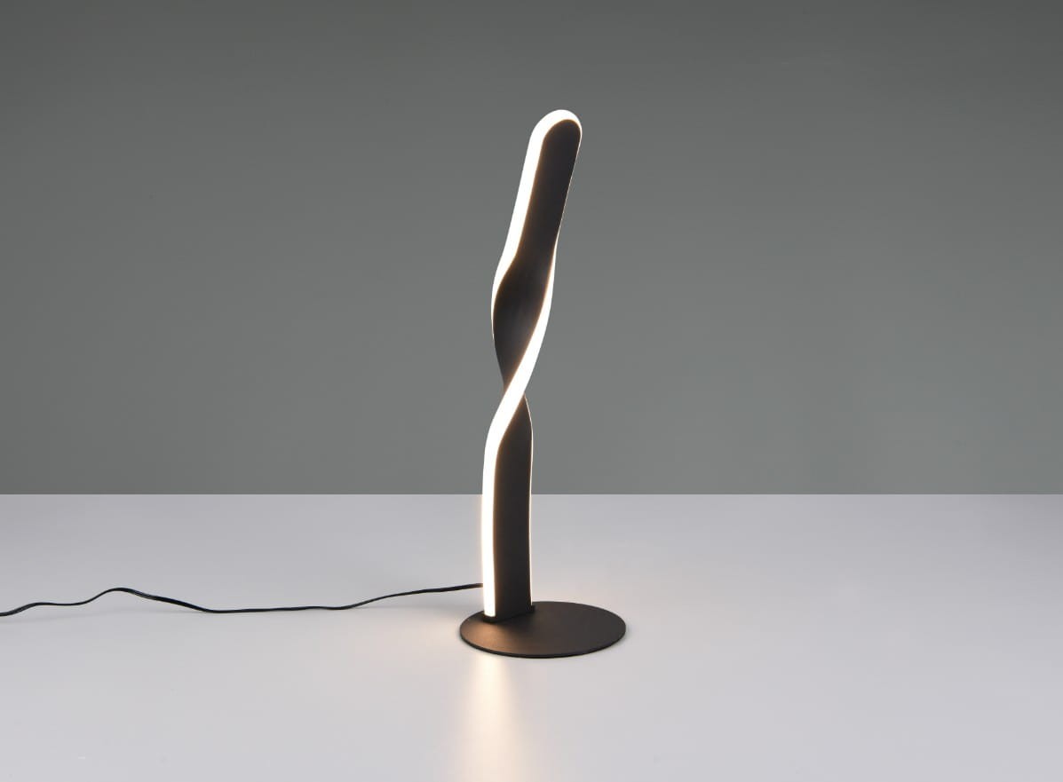 Lampa stołowa Ginko w kolorze czarnym z LED o mocy 10W. Ma nowoczesny, spiralny kształt z podświetloną krawędzią. Ustawiona pionowo na okrągłej podstawie, z widocznym kablem zasilającym. Tło w odcieniu szarym.