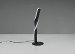 Lampa stołowa Ginko w kolorze czarnym, wykonana z metalu, o wąskiej, zakrzywionej podstawie. Ujęcie frontalne ukazuje smukły kształt z białym akcentem wzdłuż krawędzi. Produkt leży na białym stole, z widocznym przewodem zasilającym.