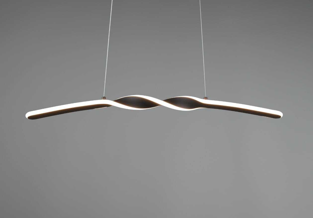 Lampa wisząca Ginko w kolorze czarnym, o prostym, wydłużonym kształcie z delikatnym, falistym wzorem. Wyposażona w jedno źródło światła LED o mocy 18W. Zawieszona na cienkich linkach, prezentuje nowoczesny design. Tło zdjęcia szare.