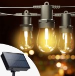 Girlanda solarna o długości 20 m w kolorze czarnym, z 20 żarówkami LED E27 1W. Widoczne żarówki w kształcie kropli, zawieszone na metalowej linki. Obok panel słoneczny, zapewniający zasilanie. Tło w rozmytych kolorach, tworzące atmosferę.