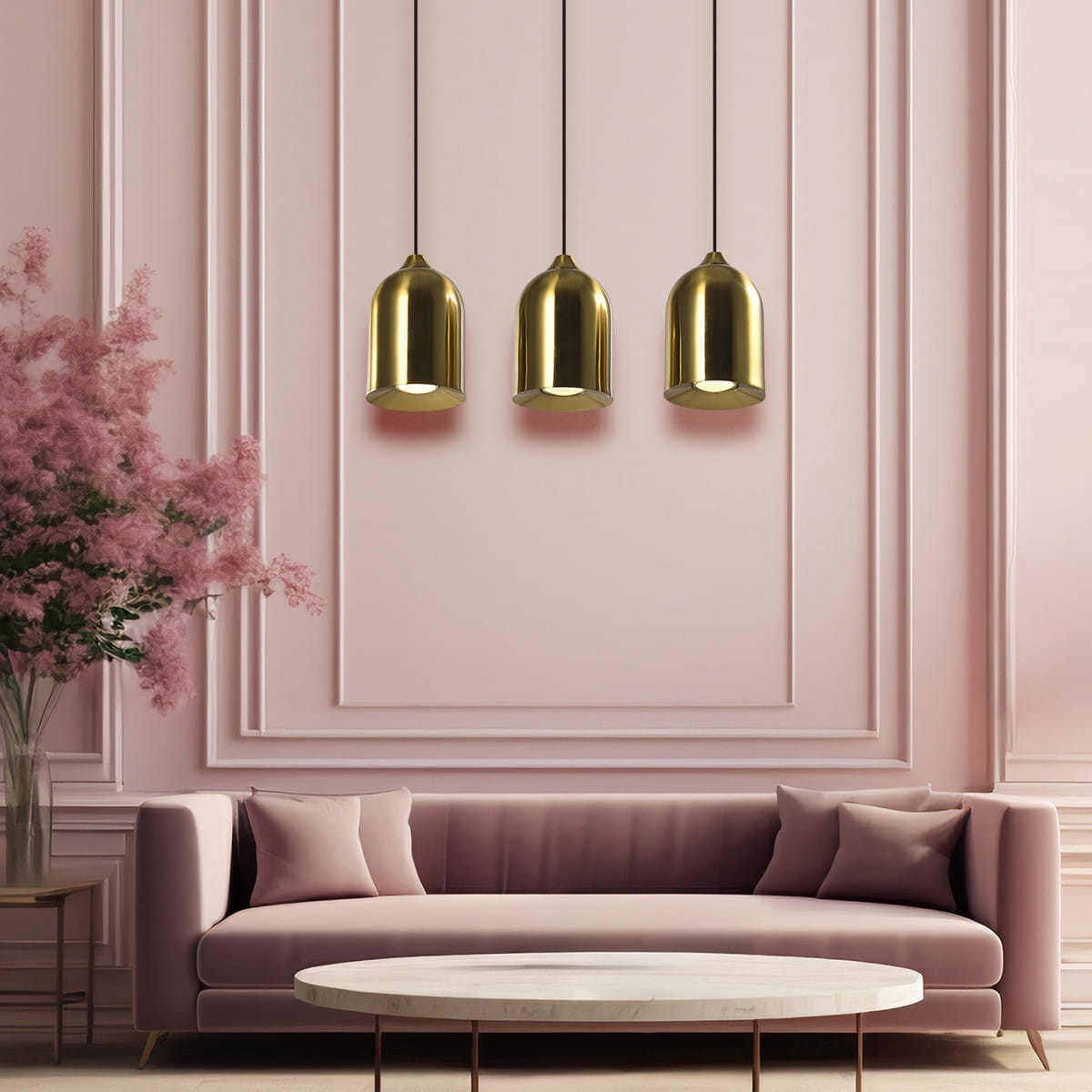 Lampa wisząca Nilo 3xGU10 w kolorze złotym, składająca się z trzech metalowych kloszy w kształcie dzwonu, zawieszonych na czarnych przewodach. Produkt umieszczony nad różowym sofą w eleganckim wnętrzu z różowymi ścianami.