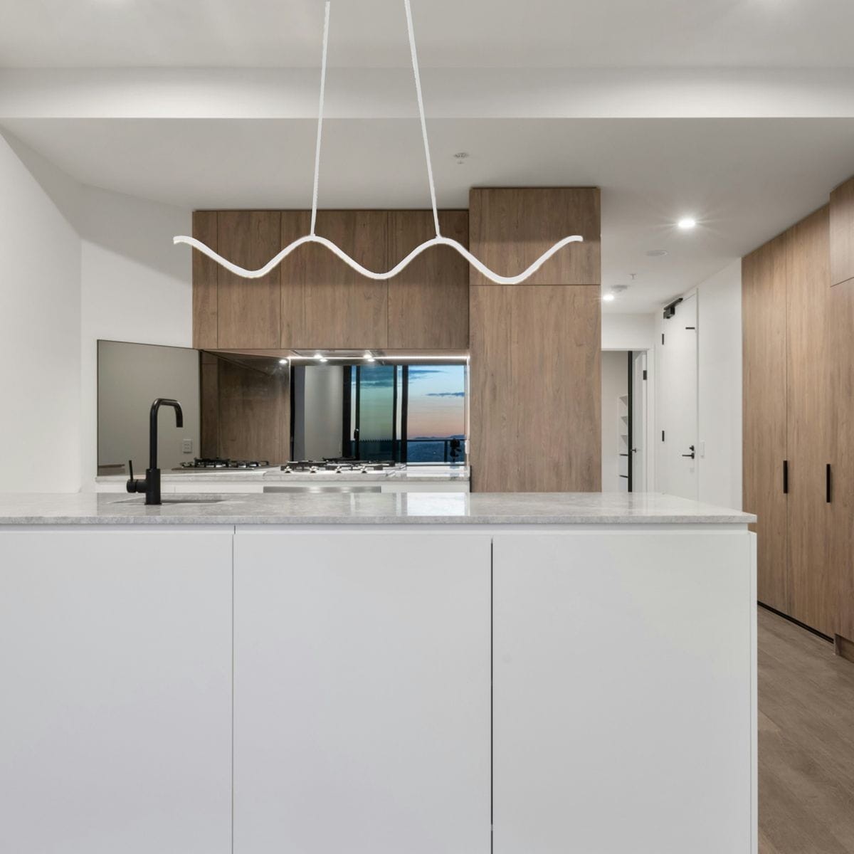 Lampa wisząca LED Zigzag w białym kolorze o mocy 13W, zawieszona w nowoczesnej kuchni. Ujęcie z góry ukazuje falisty kształt lampy oraz minimalistyczne wnętrze z drewnianymi szafkami i blatem z jasnego kamienia.