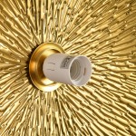 Kinkiet Sun M w złotym kolorze z fakturą w kształcie promieni. Widoczny gwint E27 w białym kolorze. Ujęcie z bliska, pokazujące detal montażu na tle złotej dekoracji.