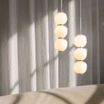 Lampa wisząca Perla LED o mocy 12W, temperatura barwowa 3000K, z trzema kryształowymi kulami w kolorze białym zawieszonymi na złotych mocowaniach. Ujęcie z boku, w tle widoczna fakturowana ściana.