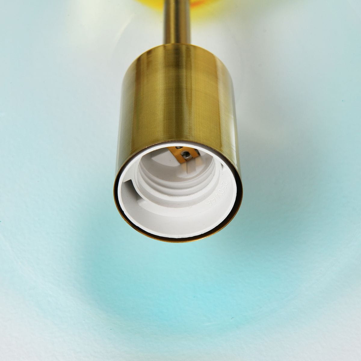 Lampa wisząca Pastello 1xE27 w kolorze złotym, z widocznym gniazdem w kolorze białym. Ujęcie z bliska, pokazujące detal mocowania oraz fakturę materiału. Tło w odcieniach niebieskiego.