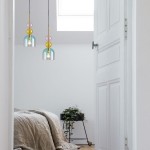 Lampa wisząca Pastello 1xE27 w kolorze złotym i niebieskim, z przezroczystym kloszem oraz dekoracyjnymi kulami w odcieniach różu, żółci i niebieskiego. Zawieszona w jasnym pomieszczeniu, nad łóżkiem, obok rośliny w doniczce.