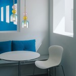 Lampa wisząca Pastello 1xE27 w kolorze złotym i niebieskim, z przezroczystym kloszem i dekoracyjnymi kulkami w odcieniach różu i złota. Ujęcie z boku, zawieszona nad okrągłym, białym stołem w minimalistycznym wnętrzu z niebieskimi poduszkami.