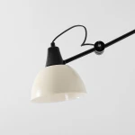 Kinkiet Aida z metalowym kloszem w kolorze kremowym, zawieszony na czarnym ramieniu. Widok z boku, zbliżenie na detal klosza i mocowania. Prosty design, idealny do nowoczesnych wnętrz.