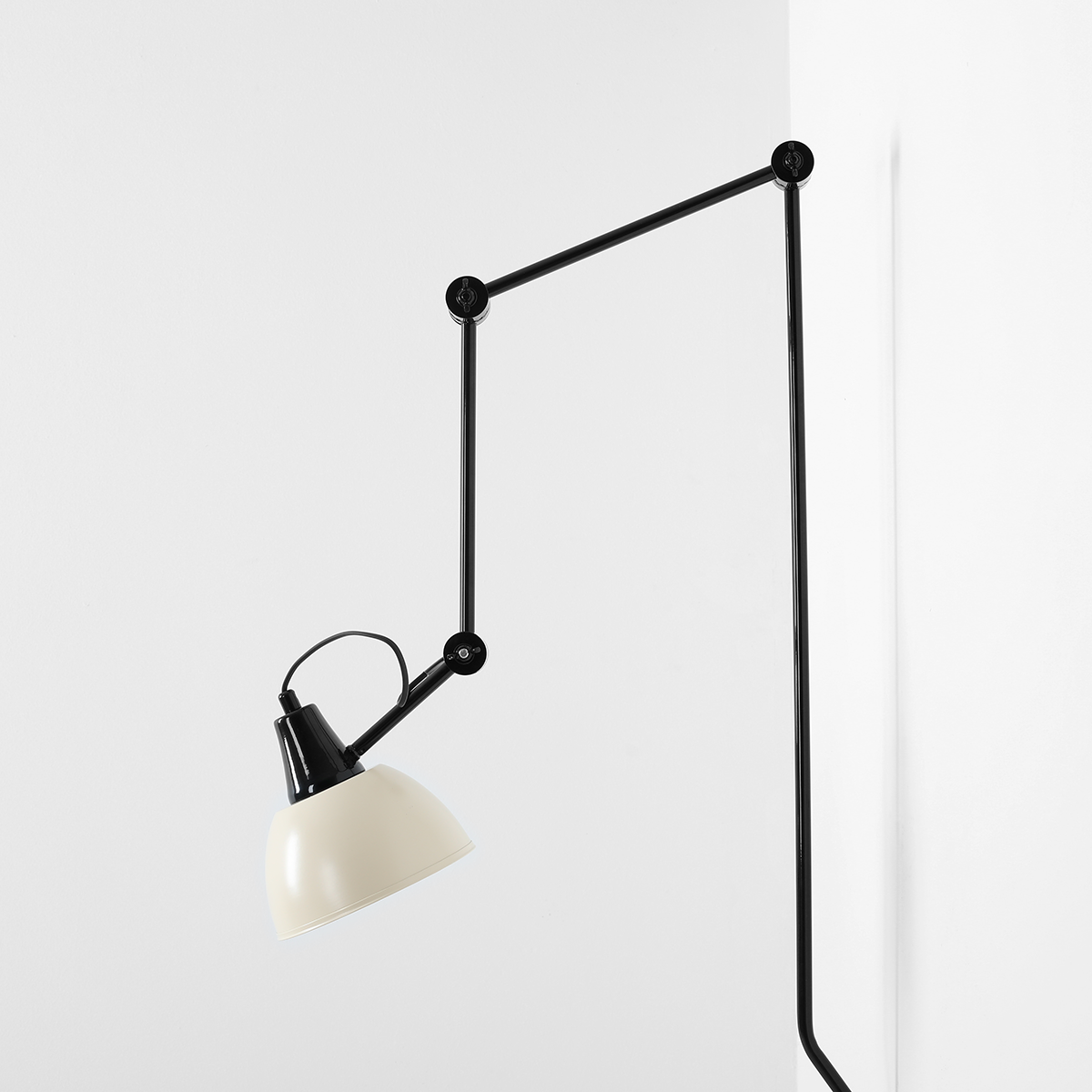 Kinkiet Aida z czarnym metalowym ramieniem i kremowym kloszem, zamontowany na ścianie. Ujęcie z boku, pokazujące kąt nachylenia klosza i detale konstrukcji. Prosty, nowoczesny design, idealny do różnych wnętrz.