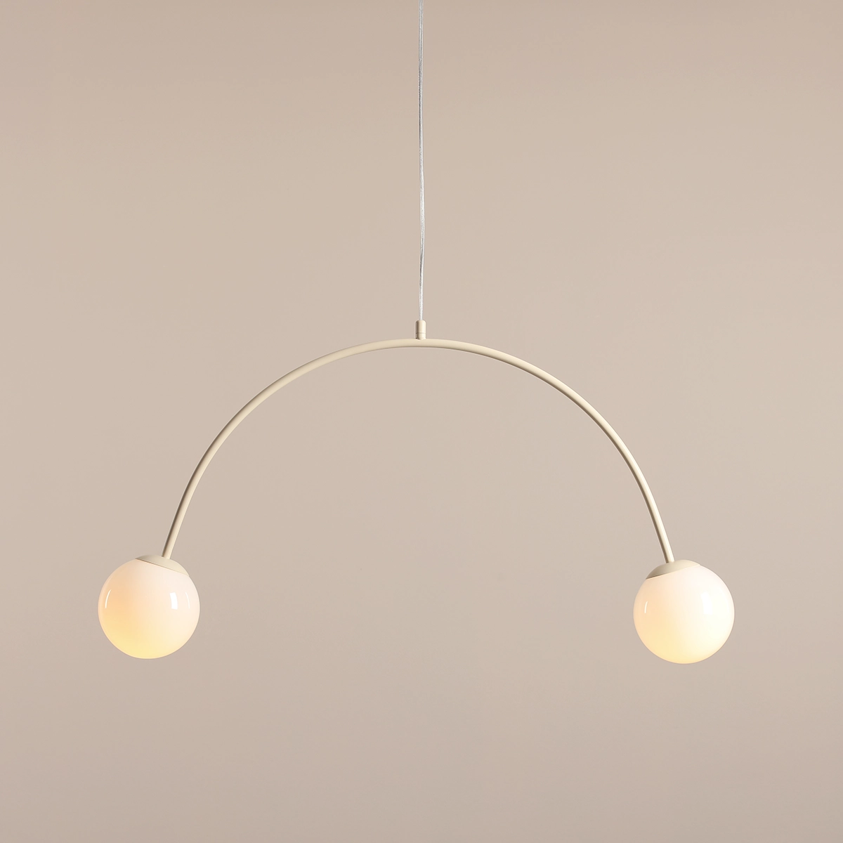 Lampa wisząca Una Cream z dwoma kulistymi kloszami, wykonana w odcieniu kremowym. Kształt łuku z metalowym stelażem, zawieszona na cienkim przewodzie. Klosze emitują ciepłe światło, co tworzy przytulną atmosferę.