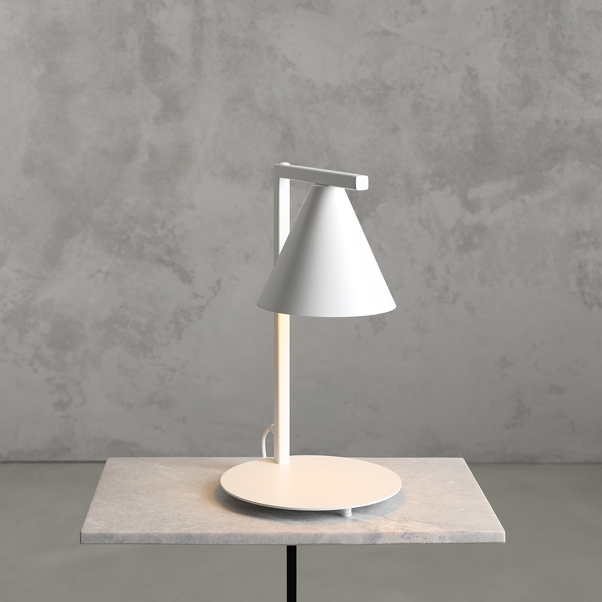 Lampa stołowa Form White z kloszem w kształcie stożka, wykonana w białym kolorze, z okrągłą podstawą. Ujęcie z boku, produkt stoi na szarej powierzchni. Widoczny przewód zasilający. Idealna do nowoczesnych wnętrz.