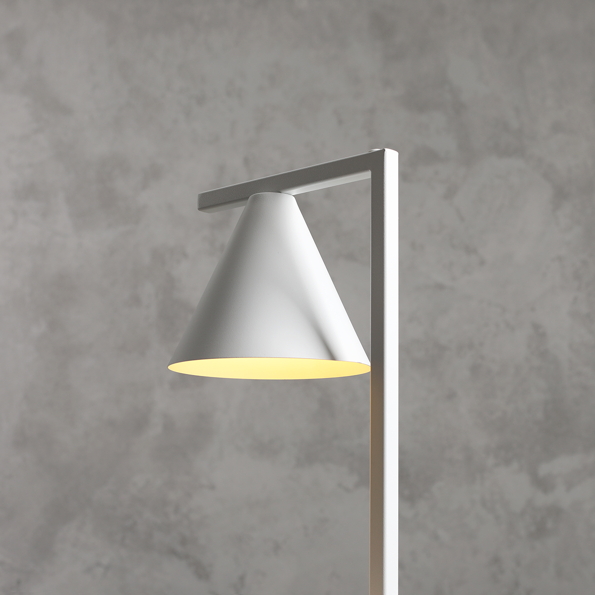 Lampa stołowa Form White z kloszem w kształcie stożka, w kolorze białym, umieszczona na prostokątnej podstawie. Klosz emituje ciepłe światło, a tło jest w odcieniach szarości. Produkt widoczny z boku, ukazujący nowoczesny design.