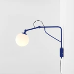 Kinkiet Soho Glass 1xE14 w kolorze kobaltowym z metalowym ramieniem i okrągłą, białą szklaną kulą. Zamontowany na ścianie, z widocznym przewodem zasilającym i włącznikiem. Idealny do nowoczesnych wnętrz.