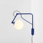 Kinkiet Soho Glass z niebieską metalową ramą i okrągłą, białą kulą ze szkła. Zawieszony na ścianie, z widocznym przewodem elektrycznym. Stylowe połączenie nowoczesności z funkcjonalnością.