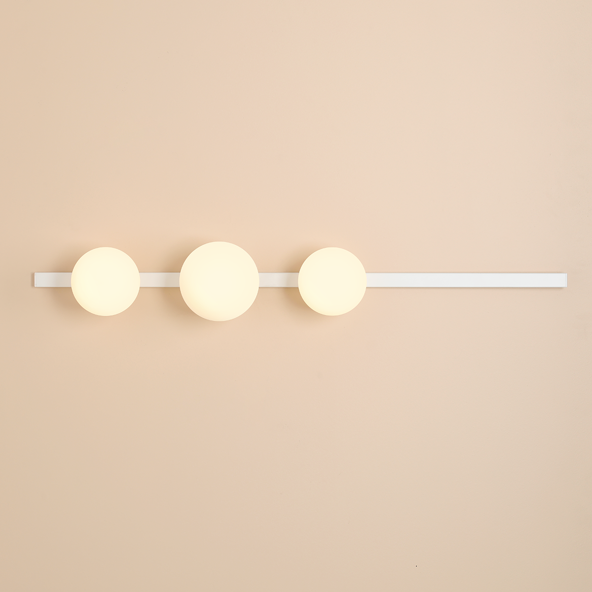 Kinkiet Garda z białą metalową ramą i trzema okrągłymi kloszami w kolorze mlecznym. Ułożony poziomo na jasnym tle, przeznaczony do montażu ściennego, dedykowany do żarówek E14 i E27.