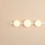 Kinkiet Garda z dwoma kulistymi kloszami E14 oraz jednym E27, umieszczony na białej metalowej listwie. Klosze mają mlecznobiałą powierzchnię, a całość jest zamontowana na gładkiej, jasnobeżowej ścianie.