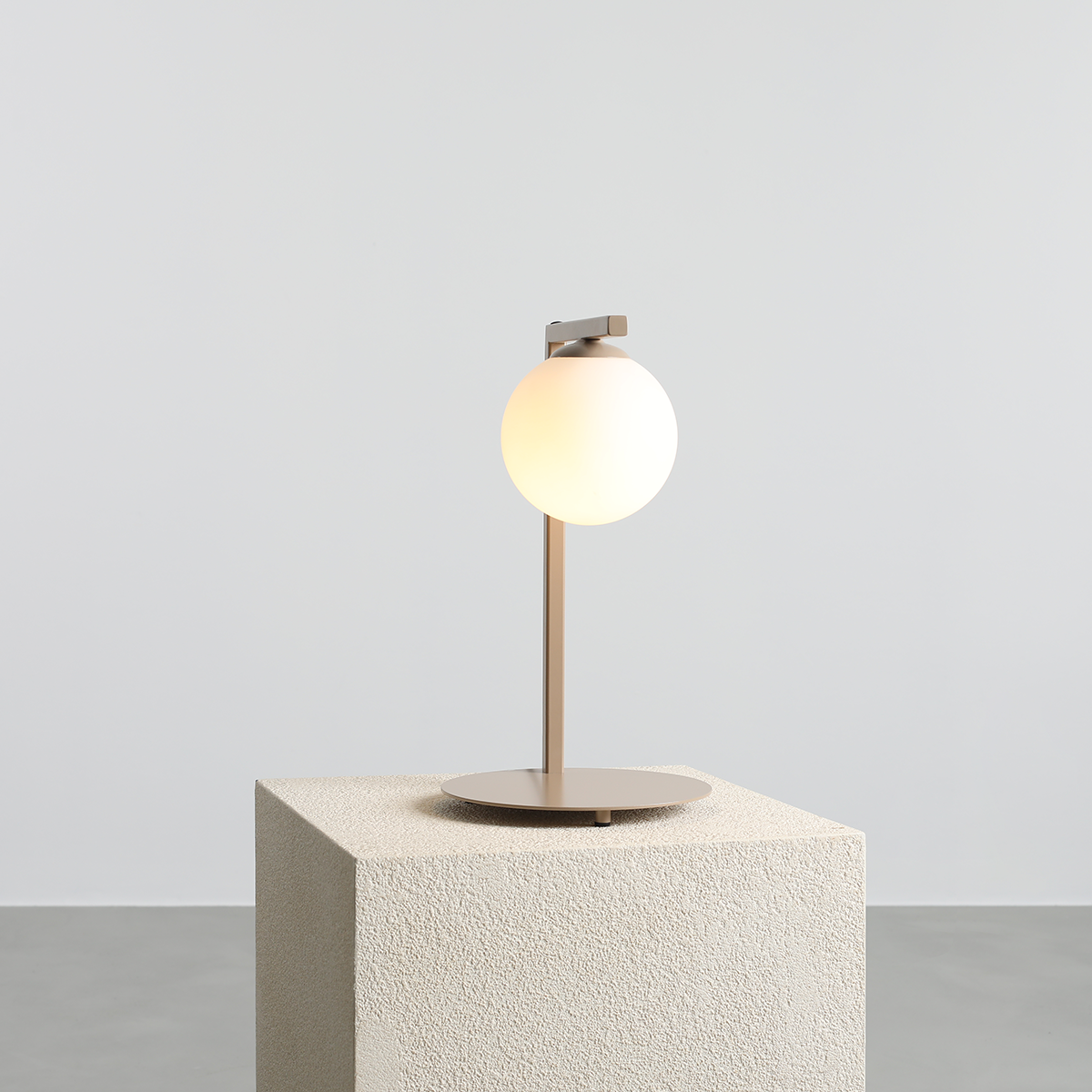 Beżowa lampa stołowa Zac z okrągłym kloszem, stojąca na okrągłej podstawie. Wysoka na około 40 cm, z metalowym stelażem i matową powierzchnią. Klosz emitujący ciepłe światło. Produkt na jednolitym tle, bez dodatkowych dekoracji.