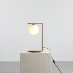 Beżowa lampa stołowa Zac z kulistym kloszem, umieszczona na okrągłej podstawie. Kąt ujęcia z boku, pokazujący prostą, nowoczesną formę oraz przewód z wyłącznikiem. Tło jasne, jednolite, podkreślające minimalistyczny design.