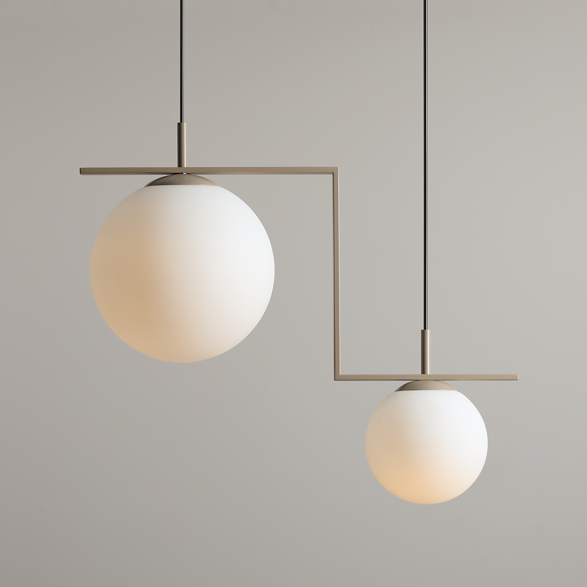 Beżowa lampa wisząca Zac II z dwiema kulistymi kloszami z mlecznego szkła, zawieszona na cienkich czarnych linkach. Klosze mają różne rozmiary, a ich geometryczny kształt podkreślony jest metalowym stelażem.